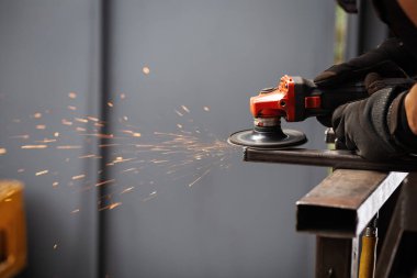İş masasında metal profiliyle çalışan profesyonel bir kumaş işçisi. Endüstriyel atölyede elektrikli bir öğütücü var. Kesme ya da temizleme mümkün.