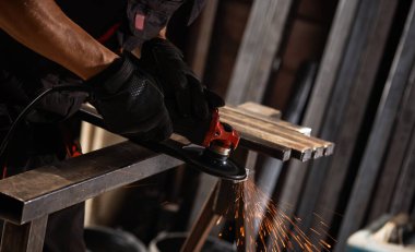 İş masasında metal profiliyle çalışan profesyonel bir kumaş işçisi. Endüstriyel atölyede elektrikli bir öğütücü var. Kesme ya da temizleme mümkün.