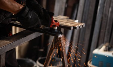 İş masasında metal profiliyle çalışan profesyonel bir kumaş işçisi. Endüstriyel atölyede elektrikli bir öğütücü var. Kesme ya da temizleme mümkün.