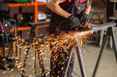 İş masasında metal profiliyle çalışan profesyonel bir kumaş işçisi. Endüstriyel atölyede elektrikli bir öğütücü var. Kesme ya da temizleme mümkün.