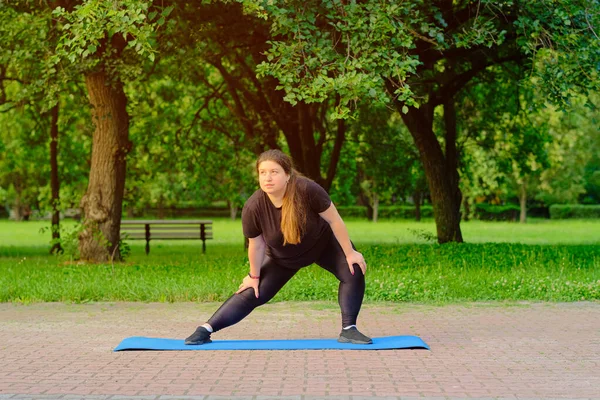 Sağlık, fitness ve spor konsepti. Genç ve iri yapılı kahverengi kadın parkta paspas üzerinde egzersiz yapıyor, fazladan kilo verecek, güçlenecek ve zinde olacak, dayanıklılık egzersizi yapacak.