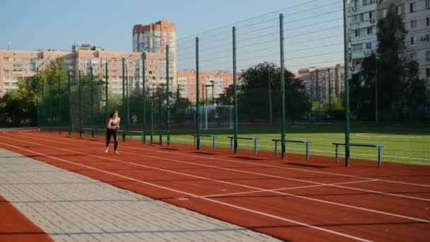 一个年轻的女人沿着一条红色的橡胶跑道奔跑 女运动员在城市里做有氧运动 女运动员在城市公园里慢跑 — 图库视频影像