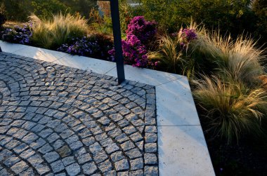 Sonbahar çiçekleri, uzun ömürlü otlar ve siyah taş kaldırımlı bir meydanda, granit kaldırımlar, sonbahar mor beyaz ve sarı astlar ve şehir parkında adaçayı ile süslenmiş otlar.