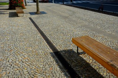Kare şeklindeki kafes, bir ağaç gövdesi için dairesel bir delik, kaldırımlı bir meydanın ortasında ya da bir çatı katında. Altın bölmeli çelik paspas, süs parkı, döşeme, asfalt.
