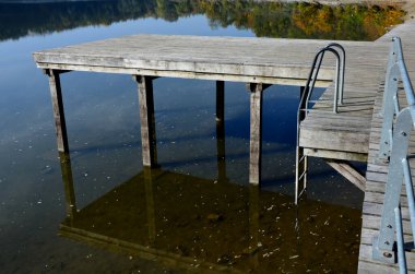 Su kenarında doğal ahşap sıralı ahşap banklar olan ahşap oturma alanı. Göletin yanındaki terasta piknik tezgahı ve kafe gibi yuvarlak masalar var. Liman iskelesi ördeklerle gölün yukarısına çıkıyor.