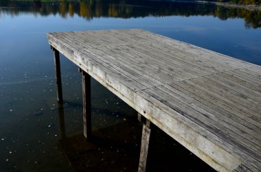 Su kenarında doğal ahşap sıralı ahşap banklar olan ahşap oturma alanı. Göletin yanındaki terasta piknik tezgahı ve kafe gibi yuvarlak masalar var. Liman iskelesi ördeklerle gölün yukarısına çıkıyor.