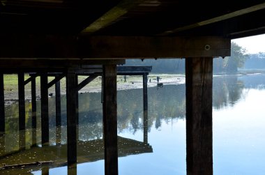 Su kenarında doğal ahşap sıralı ahşap banklar olan ahşap oturma alanı. Göletin yanındaki terasta piknik tezgahı ve kafe gibi yuvarlak masalar var. Liman iskelesi ördeklerle gölün yukarısına çıkıyor.