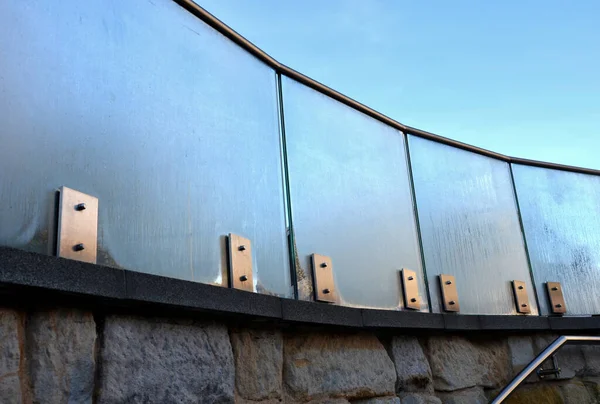 railing of a luxury house consisting of glass panels fastened with gray metal stainless steel paneling. the milky frosted glass barrier gives an airy impression. polished metal cover