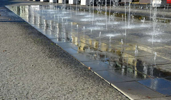 正方形花岗岩铺筑在人行道上的一条狭长地带 水喷出交替喷出的高度 水的特征直接从公园里的鹅卵石正方形中产生 湿地砖木板人行道 — 图库照片