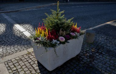 Gri bir saksı dikdörtgen şeklindedir. Çiçek saksısı, bir meydanda ya da bir parkta uzun ömürlü çiçeklerle doludur. Çelik, beton, adaçayı, çalılık, granit silindir, güneşli