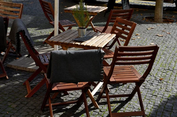 Kafe terasında ahşap bir masa ve teneke kutuda bir çiçek. Soğuğa yakalanan ziyaretçileri örtmek için arkada battaniyeler olmalı. Sonbahar terasında kahve, kasaba meydanı.