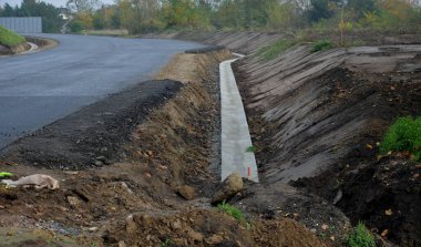 Yeni inşa edilmiş bir yol, üst üste dizilmiş perdeli ve asfalt halı katmanlarını görebilirsiniz. Çevresindeki alan beton oluğu olan bir hendeğe saplanmış. yağmur suyu drenajı