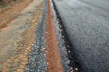 Yeni inşa edilmiş bir yol, üst üste gelen perdelenmiş ve asfalt kaplama ve delinme katmanlarını görebilirsiniz. Kenar, hendekteki toprak tarafından yavaş yavaş şekillenir, tamamlanmamış, düşer. 