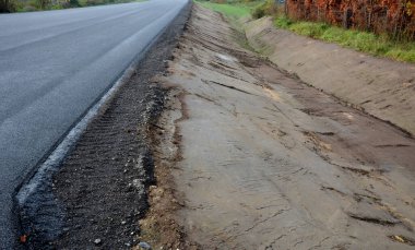 Yeni inşa edilmiş bir yol, üst üste dizilmiş perdeli ve asfalt halı katmanlarını görebilirsiniz. Çevresindeki alan beton oluğu olan bir hendeğe saplanmış. yağmur suyu drenajı