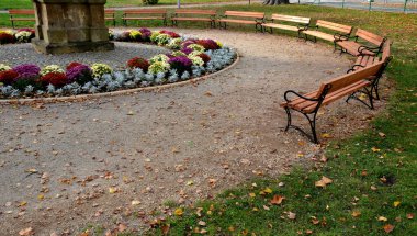 Etrafı muhteşem bir çiçek tarhıyla çevrili bir anıt ile peyzaj yapılmış bir park. Renkli sonbahar yıldızları. kaldırım taşları ve çakıl yolları ve ahşap banklar, kasaba meydanı, mor, pembe, bank, çakıl, toprak yol