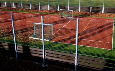 Okuldaki top oyunları için çok işlevli açık hava oyun alanı. Yeşil yapay çim, çizgileri olan plastik bir halıdan. Basketbol potaları ve futbol golleri. Ağı ve korkulukları çevreleyen, 