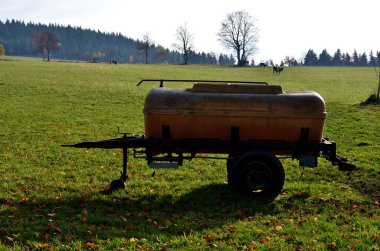 Beslenme tankının yanındaki çayırda bir inek. İneğin benekli derisi ve fermuarı andıran metal klipslerle dikilmiş bir yarası var. Ameliyat ya da karmaşık sezaryenle buzağıyı doğurtmak. tank