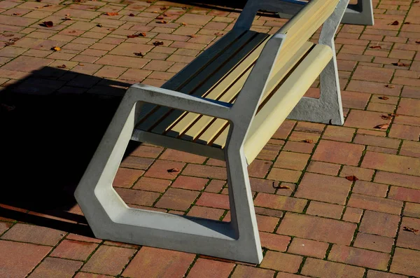 轻便混凝土公园长椅 优雅的铸造框架和轻便的木制座椅和靠背板 中午阳光下的褐色铺面正方形 园艺家具的锥形圆形 — 图库照片