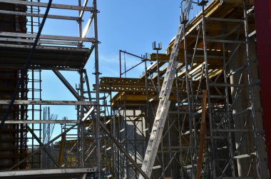 Güçlendirilmiş çelik betondan yapılmış evler depreme dayanıklıdır ve birkaç kat yüksekliğinde olabilirler. Tel örgü örülür ve karıştırıcıdan beton dökülür, mavi gökyüzü, merdiven, kırmızı, çubuk, döküm 