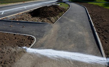 Asfaltın eski ve yeni asfalt yüzeyinin bağlantısı. Sıvı asfalt, taban ve tekerleklere yapışmasın diye silis kumuyla kaplıdır. bisiklet yolu, peyzaj ve toprak işleriyle 