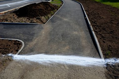 Asfaltın eski ve yeni asfalt yüzeyinin bağlantısı. Sıvı asfalt, taban ve tekerleklere yapışmasın diye silis kumuyla kaplıdır. bisiklet yolu, peyzaj ve toprak işleriyle 