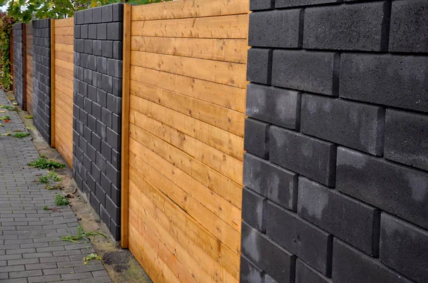 garden fencing where materials such as wood and rectangular concrete blocks are combined. between the walls are embedded pieces with planks. wet after rain