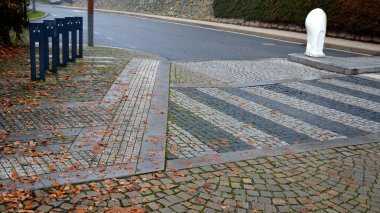 Bisiklet kulpları, ön tekerleği geçirmek için. Lazerle yakılmış bisikletçi sembolü kalın metal levha şeklinde. Farklı renklerde bloklardan yapılmış kaldırımlı yaya geçidi. Köyün merkezinde taş döşeme