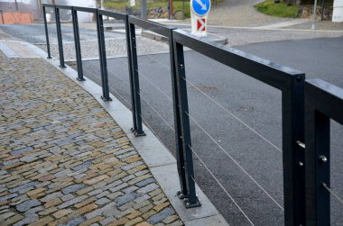 Demir parmaklıkların metal çerçeveleri yatay parmaklıklar yerine zarif paslanmaz çelik kablolarla aydınlatılır. Kavşak, kaldırım okulunu yoldan, öğrencilerden, kazadan, taş döşemeden ayırıyorlar.