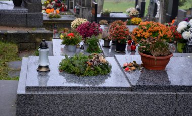 Mezar süsleme sırası. Dal ve çelenk yerleştirerek, granit taş mezar taşlarını temizleyerek ve mum yakarak kış mevsimine hazırlık. Bölgenizdeki mezar taşı ve taş işçiliği. İğne kapağı