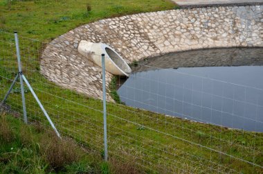 behind a wire fence is a sluice gate. the slide can be set to a certain water level. it holds back the flushes from the sewage system. reservoir as a source of water for making snow on the ski slopes  clipart