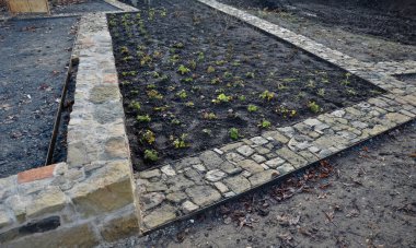 Taş kaldırım, iki çelik kaldırım taşının arasındaki çakıl döşemesinde kurumuş. Kum taşı ve yanmış tuğla parçaları kırsal bir his veriyor. Bitki bahçesindeki dar park yolları, alçak, tutucu, yanmış