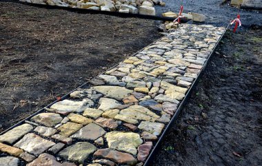 Taş kaldırım, iki çelik kaldırım taşının arasındaki çakıl döşemesinde kurumuş. Kum taşı ve yanmış tuğla parçaları kırsal bir his veriyor. Bitki bahçesindeki dar park yolları, alçak, tutucu, yanmış