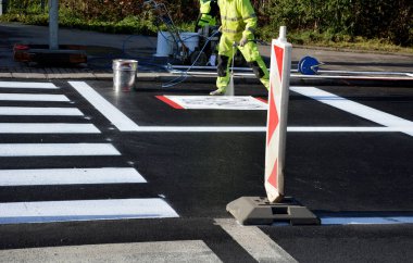 Kavşakta kavşak ve kavşakta yatay işaretler düzeltiliyor. Şablon kullanarak yeni semboller püskürtüyorlar. Sonra onu kum pigmentiyle kaplıyorlar. Tekerlek değil, yansıtıcı yeşil giysi.