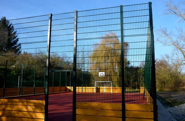 stock image multifunctional outdoor playground for ball games at school. green artificial turf from a plastic carpet with lines. basketball hoops and soccer goals. around the grabbing high net and guardrails 