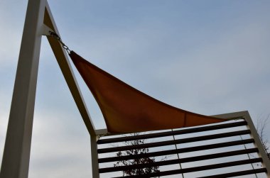 Sarı tuval gerildi, restoranın terasında güneş ve yağmurdan gölgelendi, çocuk parkında, gezinti alanında. Tahta gri kirişli pergola, beyaz metal çelik üzerinde, bağlanıyor, bağlanıyor, bağlanıyor