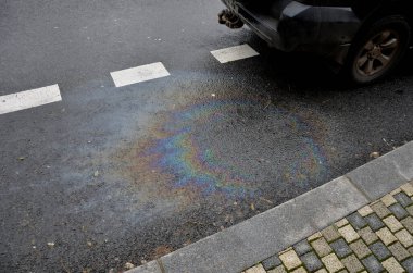 Araba motorundaki yağ lekeleri yüzünden. Yağmurdan sonra yağan yağ, gökkuşağı yansımaları kırıcı güneş tayfı oluşturur. Siyah arka plan otoparkında güzel renk mozaiği, soyutlama, ekoloji