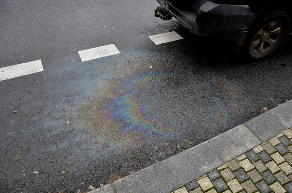 oil stains from leaks in the car engine. oil after rain makes spots with rainbow reflections refractive sun spectrum. beautiful color mosaic on black background parking lot, abstraction, ecology
