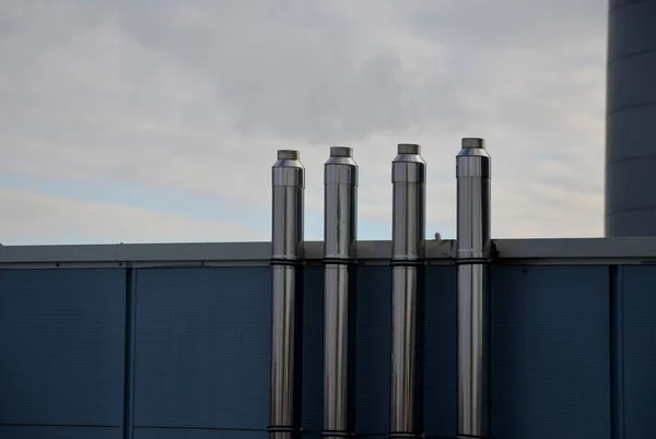 Industrial white building with sheet metal facade of repeating rectangle paneling. on wall are two silver-shiny chimney pipes with a curved and bevelled stainless steel pipe. gas heating turbo boiler