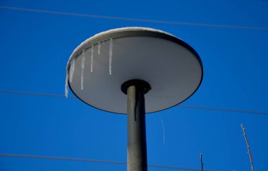 Tabak şeklinde sokak lambası. Sarkıtın kenarına dairesel bir ışık yerleştirilmiş. Gri sütun, mavi gökyüzü