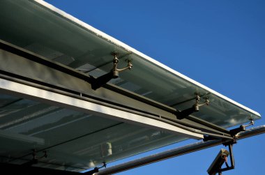 Otobüs durağı camlanıyor. Metal yapıya birkaç noktadan cam tepe örtüsü bağlanmış. Gökyüzü arasındaki boşluklar güneş ışığından korunmak için noktalar, karla kaplı, buzlu camlar