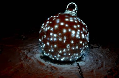 Noel temalı süsler dışarıda, karlı bir parkta, ya da açık. Yaya gezintisi. Top şeklinde metal iskelet ve fiyonk şeklinde bir hediye..