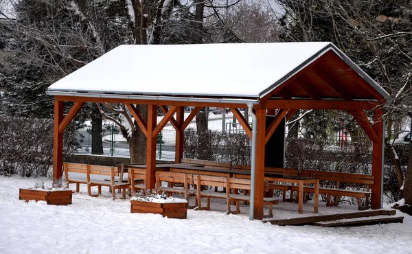 outdoor pergola currently covered in snow. rectangle gazebo made of beams and tables and chairs inside. outdoor classroom with chalkboard. benches and under the roof galvanized sheet gutter.