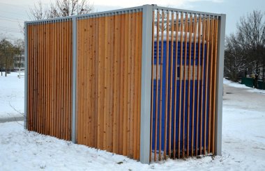 Kimyasal tuvaletler için kapanış kafesi. Görünmez plastik kutular metal bir evin içinde, çatısı düz ve duvarları tahta. Parktaki atletler ya da çocuklu anneler işeyebilir, ellerini yıkayabilir.