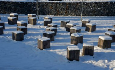 Kışın parkta ahşap bir bank. Taş ocağından taş blokları ve küpler de kaba kireçtaşı blokları. Küp şeklinde bank. meşe ağacı, bir parça, noel ağacı, dekorasyon, küre, kırmızı, cam, vida