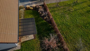 Güzel bir bahçedeki terasta tel metal sandalyeler ve oval masa gibi bahçe mobilyaları var. gri beton teras. Çimen / çiçeklendiren, süsleyen otlar,