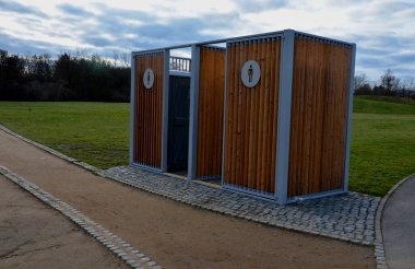 Kimyasal tuvaletler için kapanış kafesi. Görünmez plastik kutular metal bir evin içinde, çatısı düz ve duvarları tahta. Parktaki atletler ya da çocuklu anneler işeyebilir, ellerini yıkayabilir.