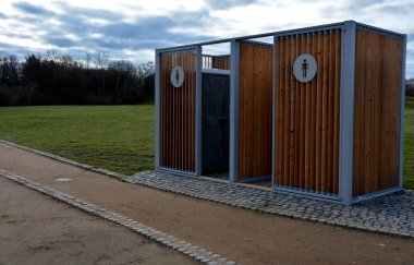 Kimyasal tuvaletler için kapanış kafesi. Görünmez plastik kutular metal bir evin içinde, çatısı düz ve duvarları tahta. Parktaki atletler ya da çocuklu anneler işeyebilir, ellerini yıkayabilir.