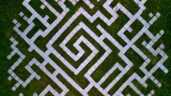 floor plan of a garden with a mosaic of tiles in the shape of a twisted digital maze of concrete square tiles. lawn with path for children