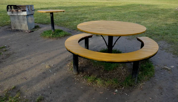 a circle-shaped camping bench with a table around it. yellow. barbecue place on the meadow in the empty spring park