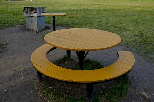 a circle-shaped camping bench with a table around it. yellow. barbecue place on the meadow in the empty spring park